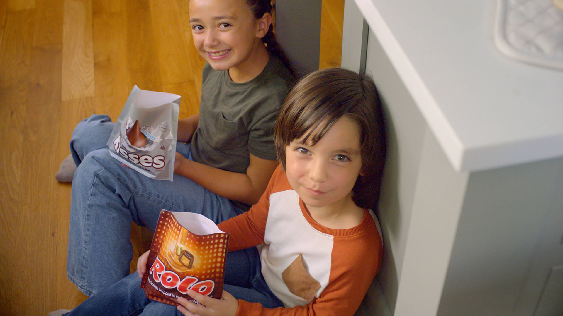 kids sitting on kitchen floor holding bags of hersheys kisses and rolo creamy caramels